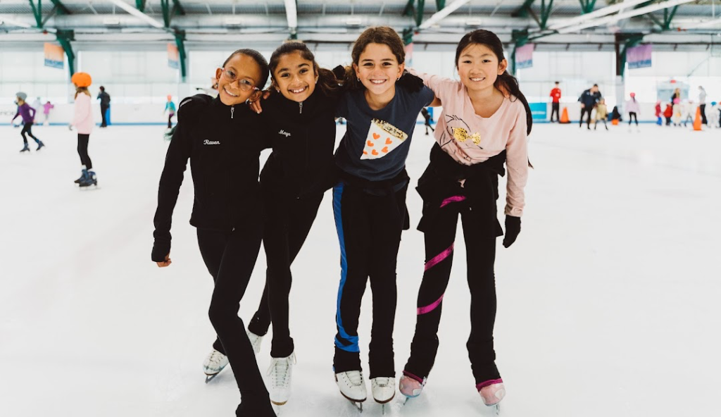 Group of kids ice skating at Chelsea Piers Sports House in Manhattan, smiling and posing together on the indoor ice rink.