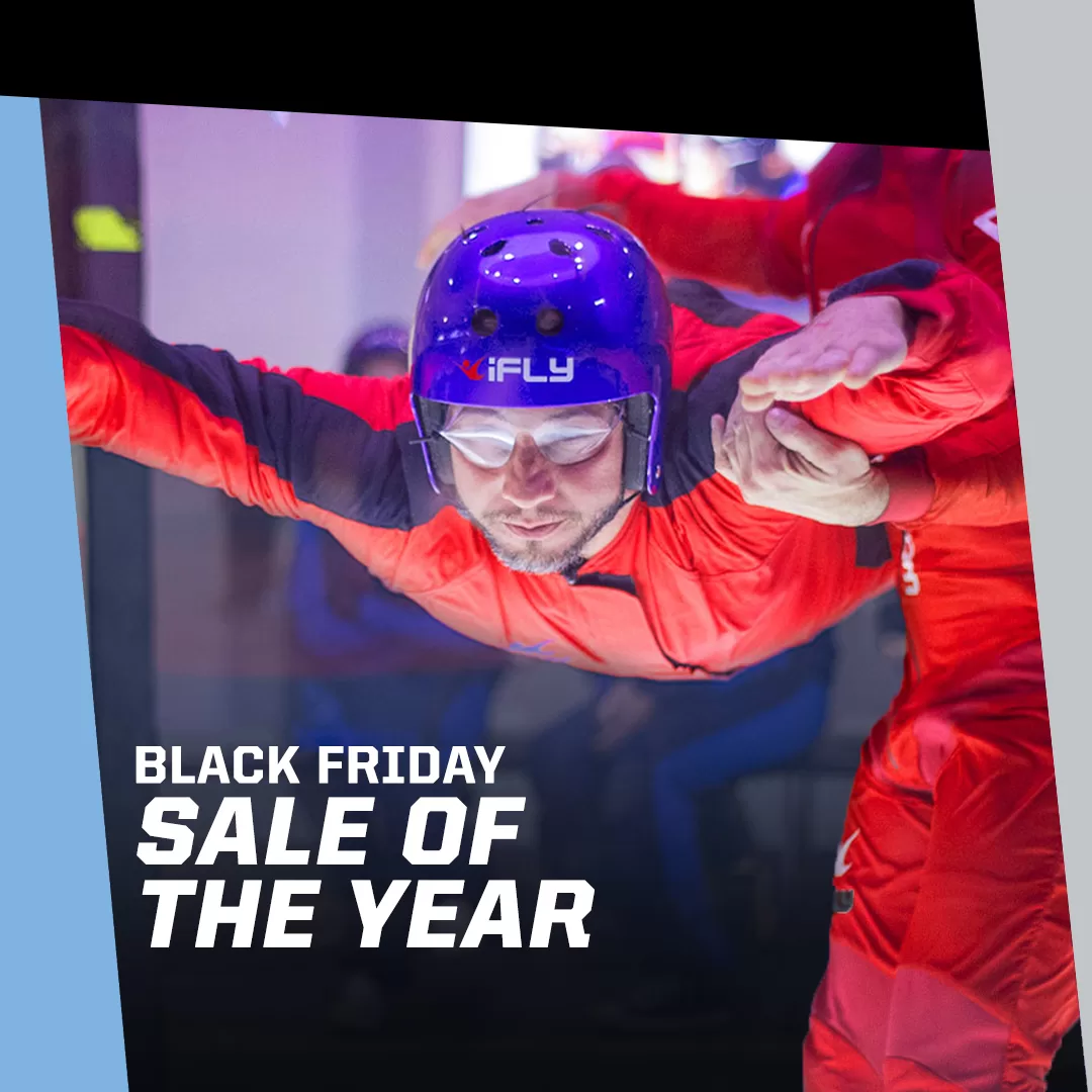 An indoor skydiver in a red suit and blue helmet with the iFLY logo, experiencing the thrill of flying during the Black Friday Sale of the Year.